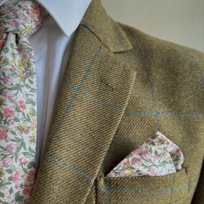 Brown tweed jacket with floral pocket square and tie against a neutral background