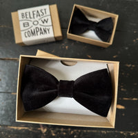 Black bow tie in a box with 'Belfast Bow Company' packaging on a dark surface.